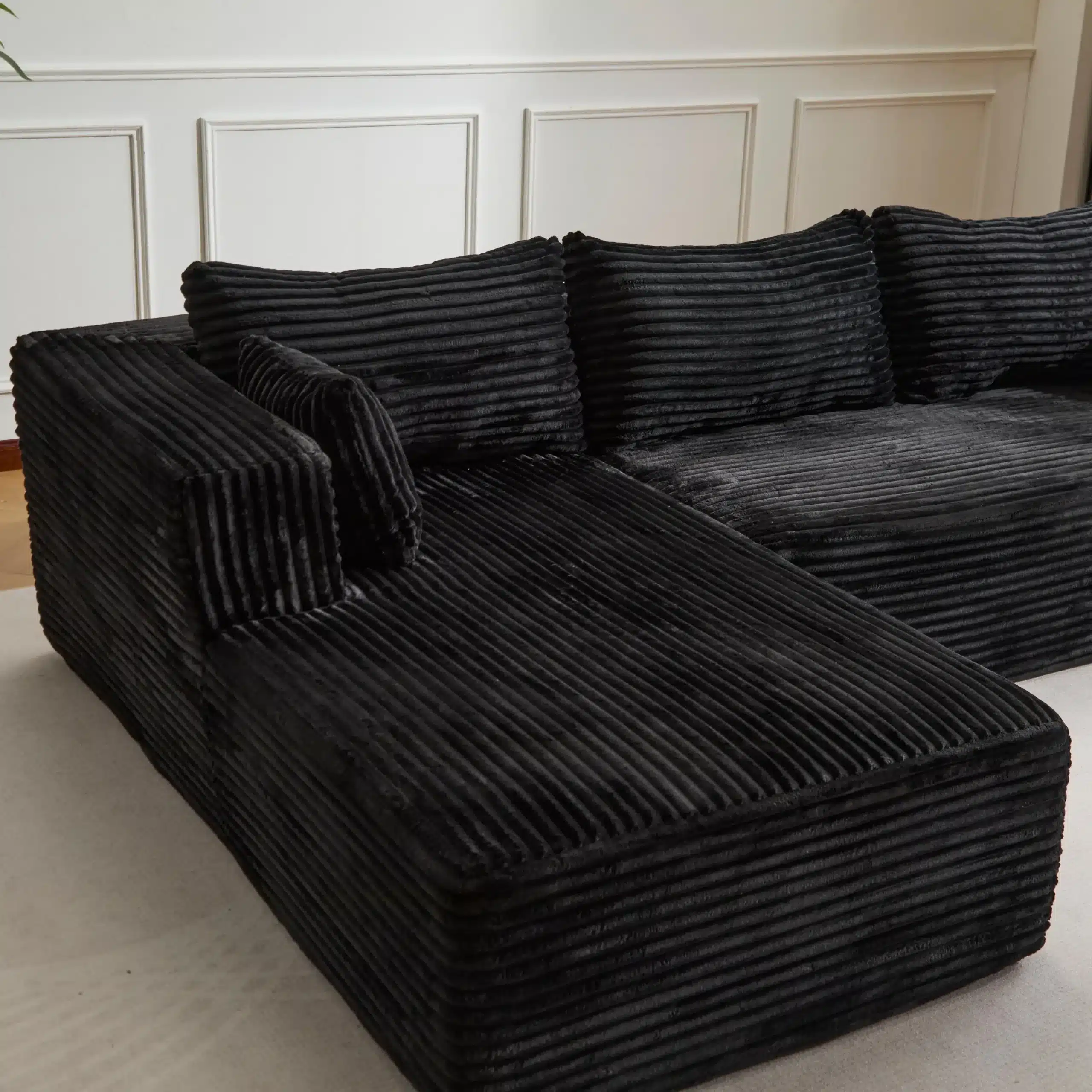 Stiilne ja kaasaegne väga mugav muuduldiivan musta värvi, millel on lameda struktuuriga velvetkumm ja mitmekülgne L-kujuline disain. Taustal on hele seinapaneel, mis lisab elegantsuse tunnetust.