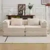 Kahe istmega diivanvoodi beežist pehmest veluurist, paigutatud stiilsesse elutuppa. Taustal valge paneelsein ja dekoratiivsed esemed puidust kummutipeal.