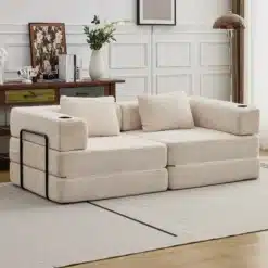 Kahe inimese diivanvoodi, valmistatud pehmest beežist sametist ja kokkupandava mehhanismiga. Diivan asub heledas, stiilses elutoas, mille puidust põrandad ning hele vaip loovad hubase ja elegantse atmosfääri. Taustal näha puidust kappi koos dekoratiivsete esemete ja valge vaasiga täidetud lilledega.