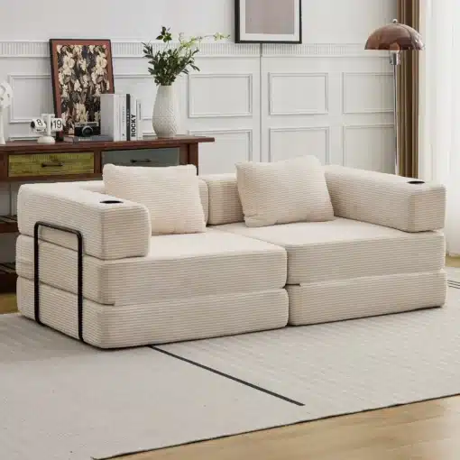 Kahe inimese diivanvoodi, valmistatud pehmest beežist sametist ja kokkupandava mehhanismiga. Diivan asub heledas, stiilses elutoas, mille puidust põrandad ning hele vaip loovad hubase ja elegantse atmosfääri. Taustal näha puidust kappi koos dekoratiivsete esemete ja valge vaasiga täidetud lilledega.