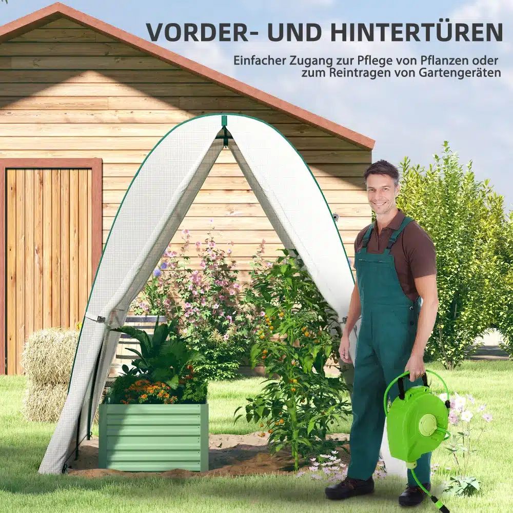 Kasvuhoone kahe ukse ja võrkvakendega 180x180x200 cm aias, mees kastekannuga, taustal puidust kuur ja lopsakad taimed.