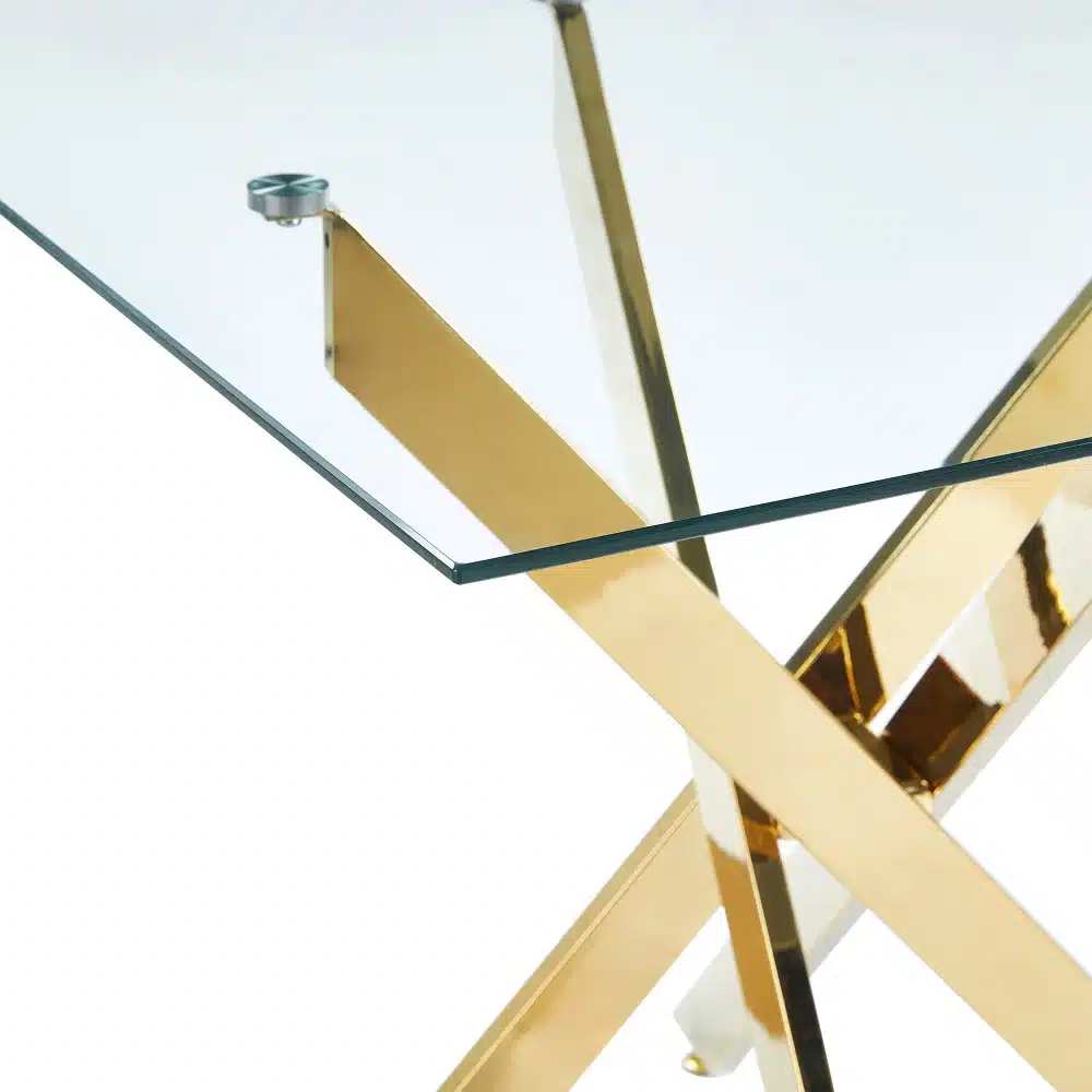 Modernne söögilaud karastatud klaasiga, mille kuldsed metalljalad ristuvad elegantselt, peegeldades valgusküllasel taustal luksust ja stiili.
