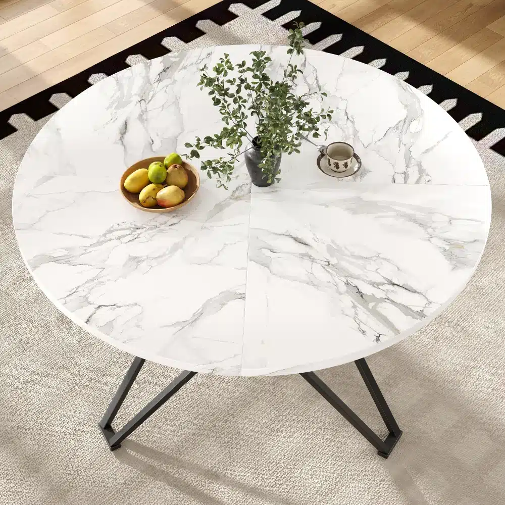 Ümmargune söögilaud marmorviimistlusega, 100x100 cm, millel asuvad puuviljakauss ja taimepott valgusküllases söögitoas, heledal vaibal.