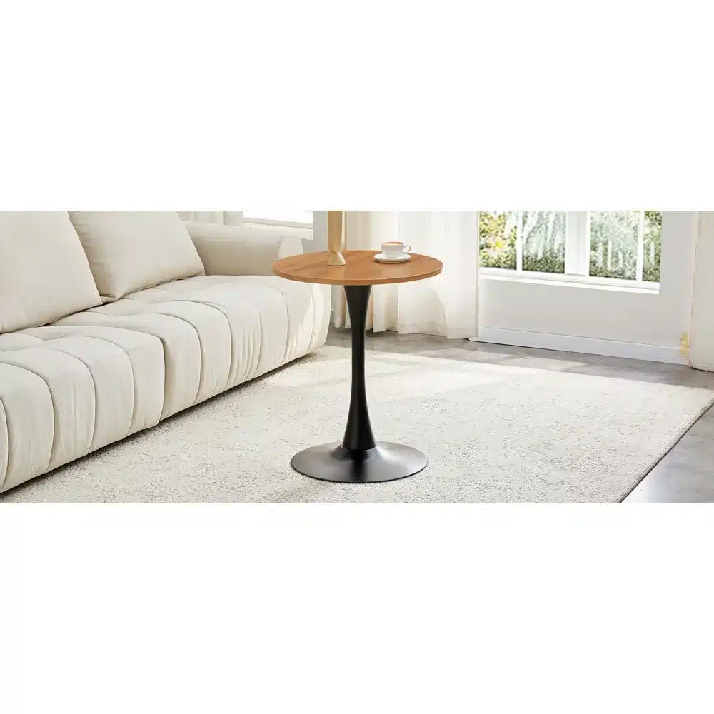 Ümmargune diivanilaud, diameetriga 60 cm, pähklipuu MDF materjalist pealislaud, kuldne jalg. Laud asub heledal vaibal, ühes ruumi nurgas. Diivan ja suur aken taustal. Ruum on helge ja modernne.