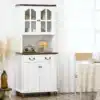Valge köögikapp klaasuste ja kahe sahtliga | E-pood Tootemaailm Valge köögikapp klaasuste ja kahe sahtliga, mis on asetatud valgusküllasesse ruumi heleda puidust põrandaga. Kapp on elegantse disainiga, varustatud tumeda puidust lauaplaadi ja messingist käepidemetega.