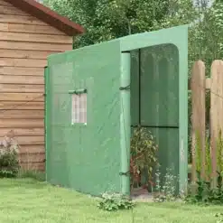 Roheline kasvuhoone UV-kaitsega, kahe ukse ja aknaga, 200x80x200, mis asetseb aias puumaja lähedal. Kasvuhoone sees on kasvavad taimed, taustal lopsakas roheline aed.