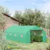 Suur roheline kasvuhoone PE kattega, mõõtmetega 6x3x2 m, seisab ilusal päikesepaistelisel aial, ümbritsetud rohelise muruga ja taimedega, taustal puidust kuur ja puid.