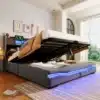 Pesukastiga voodi LED-valgustusega 160x200 USB-C-ga | E-pood Tootemaailm Pesukastiga voodi mõõtmetega 160x200, millel on modernne hall polsterdus ja LED-valgustus. Voodi on üles tõstetud, paljastades avara hoiuala. Taustal on hele tuba, mille aknast paistab roheline vaade.