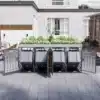Prügikastide komplekt istutusalustega, lukuga, 4 tk | E-pood Tootemaailm Neljaosaline prügikastide komplekt istutusalustega ja lukuga avatud uksega, paigutatud hallile kiviplaatidest terrassile valgete fassaadiga maja ees.