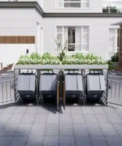 Neljaosaline prügikastide komplekt istutusalustega ja lukuga avatud uksega, paigutatud hallile kiviplaatidest terrassile valgete fassaadiga maja ees.
