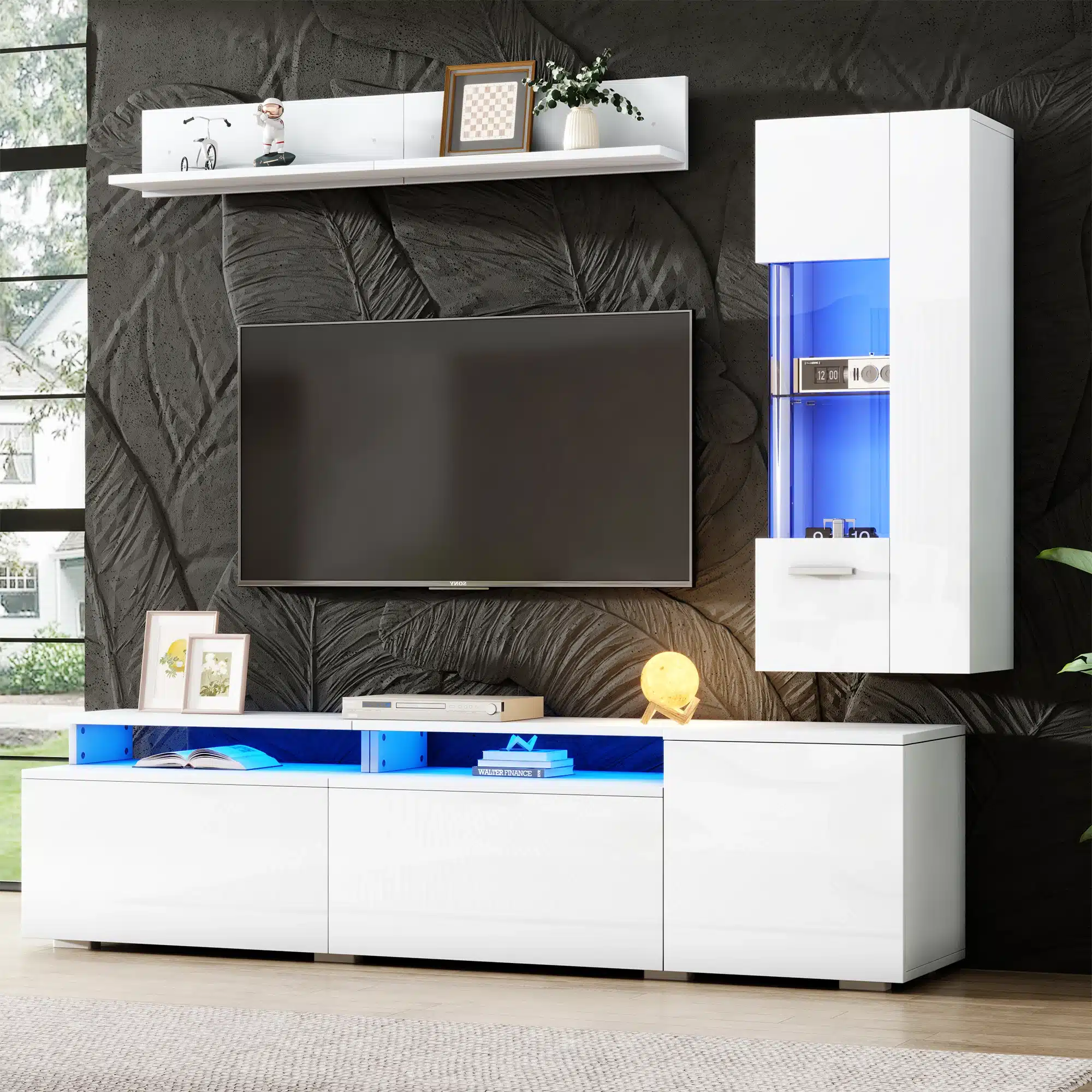 TV-elutoa komplekt LED-valgustusega, valge kõrgläige. Komplekt sisaldab elegantset valget kõrgläikega kapp-süsteemi ja riiulit koos sinise LED-valgustusega, mille taustal on musta lehemustriga seinapaneel, suure televiisori ja akna kõrval.