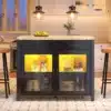 Köögilaud kapi, LED-valgusega, puidu imitatsioon | E-pood Tootemaailm Elegantne köögilaud kapi koos LED-valgusega, mille puidu imitatsiooniga töötasapind täiendab stiilset musta kapi. Klaasuksed avanevad sooja valguse sisse, rõhutades sisemist paigutust. Taustal valge köök ja ripplambid loovad koduse atmosfääri.