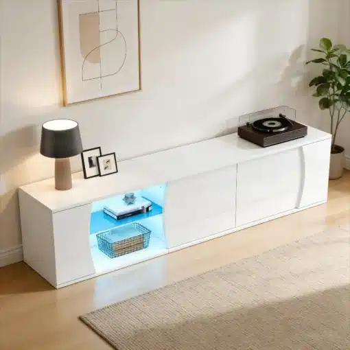TV-alus LED-valgustusega, karastatud klaas, 180 cm | E-pood Tootemaailm Valge TV-alus LED-valgustusega, mis on valmistatud karastatud klaasist ja on 180 cm pikk. TV-alus asub heledal puitpõrandal, millel on dekoratiivsed esemed, nagu raamitud pildid, lamp ja vinüülplaadimängija. Aluse keskosa on valgustatud sinise LED-valgusega, lisades modernse ja stiilse puudutuse.