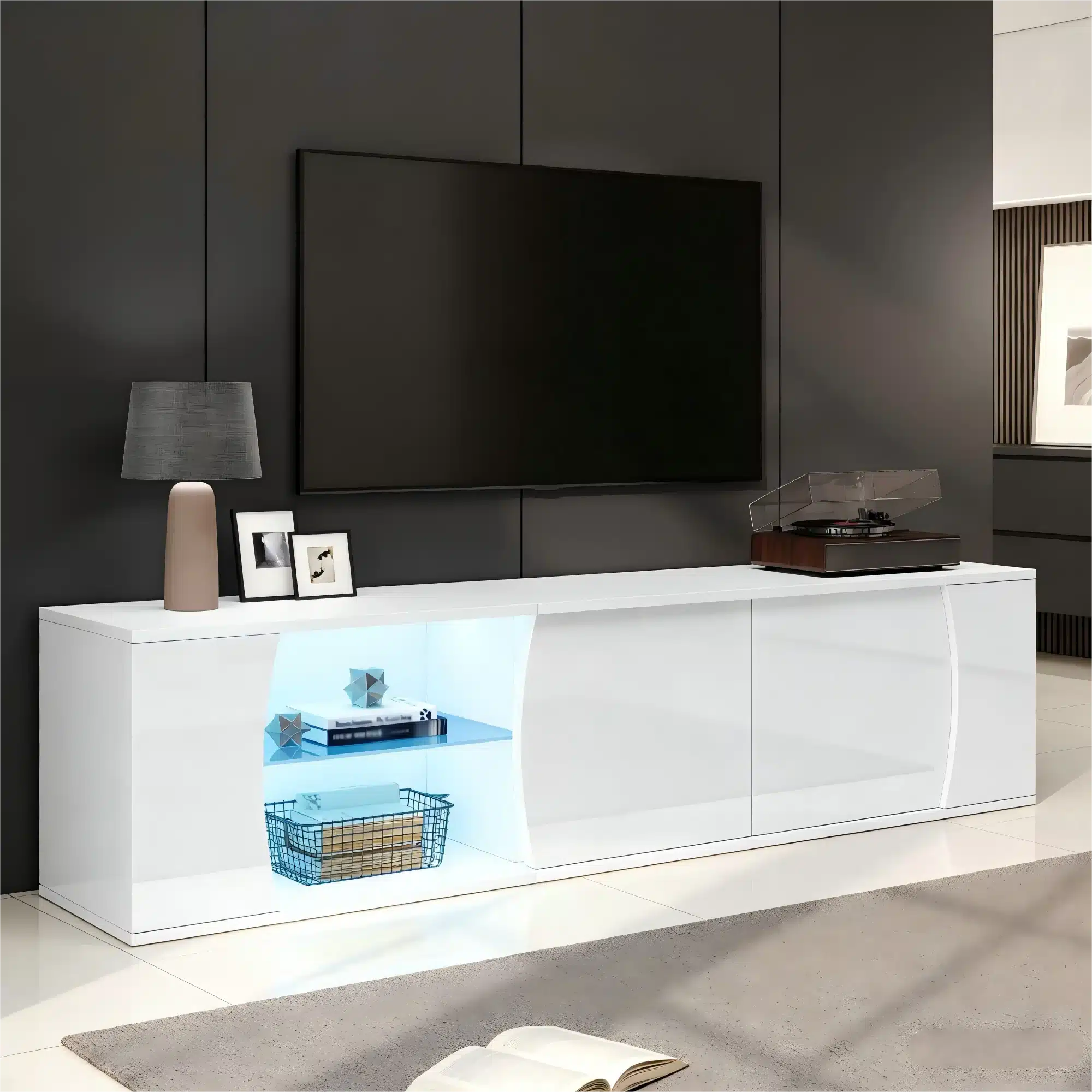 Stiilne ja kaasaegne valge TV-alus LED-valgustusega, karastatud klaasist detailid, 180 cm pikkune. Kapi ühel küljel on hele valgustatud riiul, mis on sobiv dekoratsioonide esitlemiseks. Taustal on tumedat värvi sein ja suure ekraaniga televiisor.