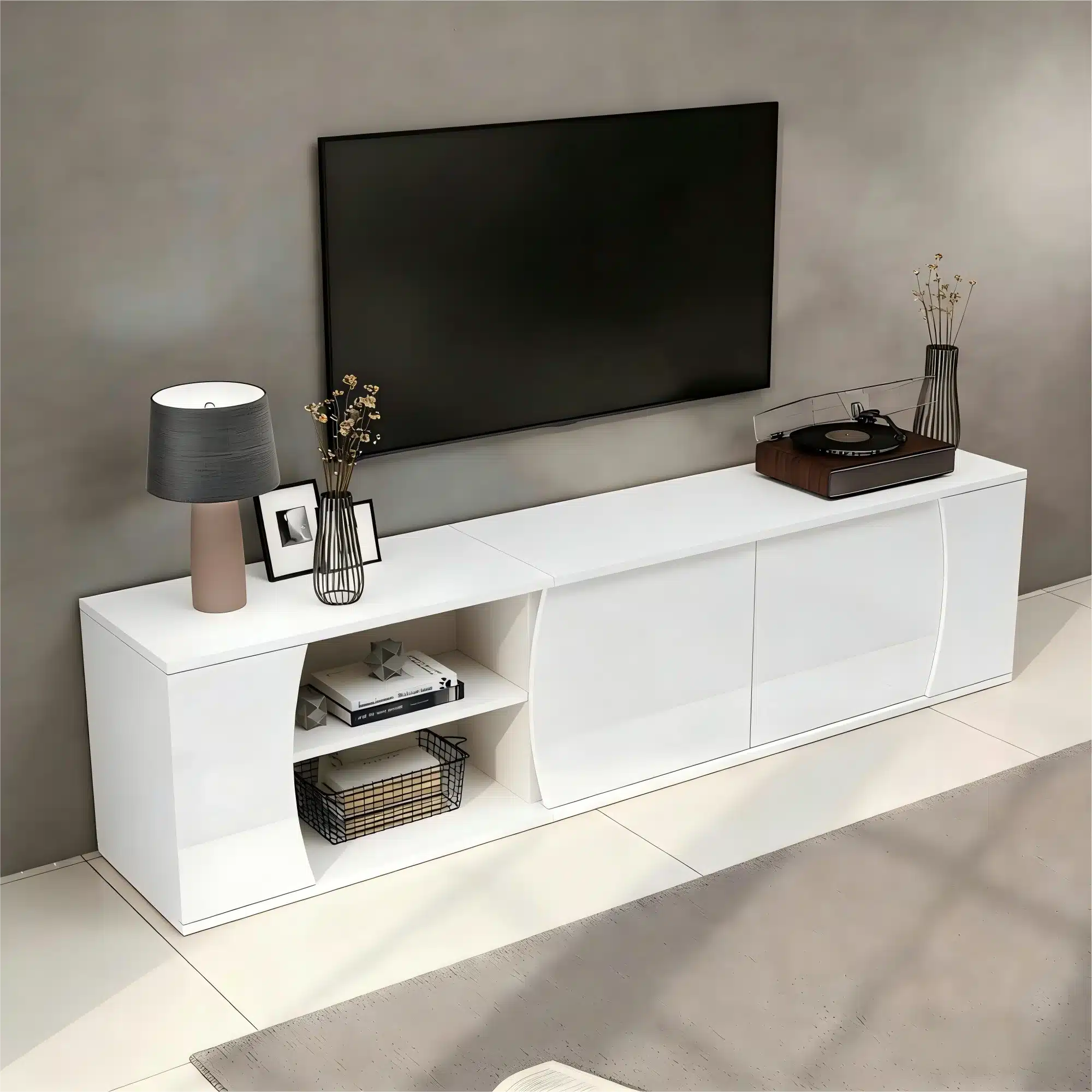 Valge TV-alus LED-valgustusega, karastatud klaasiga, 180 cm pikk. Alaosas avatud riiul, ülemisel riiulil lamp ja dekoratiivesemed. Taustal hele sein.