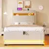 Pesukastiga voodid, USB-C ja LED, 90x200 cm | E-pood Tootemaailm Elegantses helebeežis pesukastiga voodi, mille jalutsil on LED-valgustus ja peatsis USB-C laadimisvõimalus. Voodi asub heledas magamistoas, mille seinal ripuvad kaks kunstipilti ja kell. Mööbel on paigutatud hubaselt ja stiilselt koos öökapi ja lampidega.
