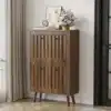Kingakapp pähklipuidust, vertikaalse soonilise pinnaga 60 cm | E-pood Tootemaailm Esik, mis sisaldab pähklipuidust kingakappi, millel on vertikaalne sooniline pind ja kõrgus 60 cm. Kapp asub heledal puitpõrandal ja selle peal on lilleseade ning kunstiteos.