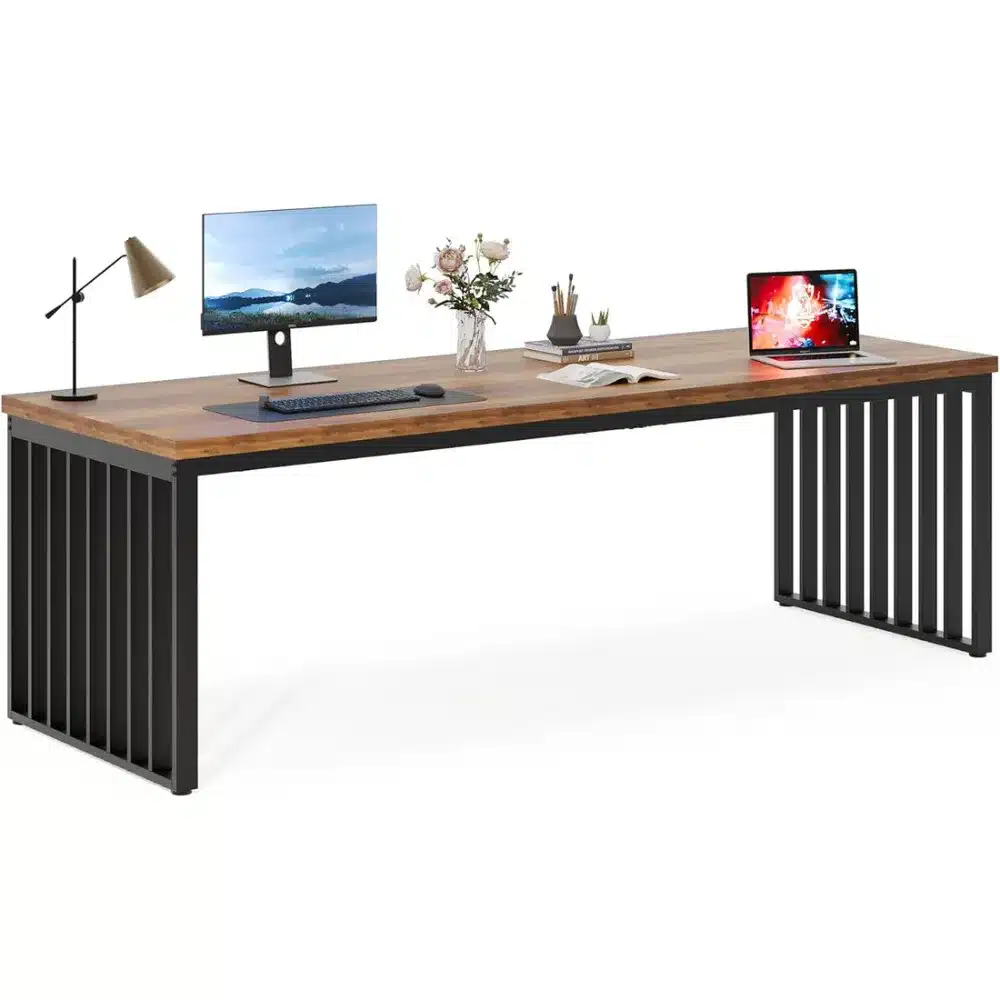 Kahe inimese kirjutuslaud pikk töölaud kodukontorisse, puitmaterjalist pealispind, metallist raam, millel on monitor, sülearvuti ja dekoratiivsed elemendid nagu lamp ja lillevaas.