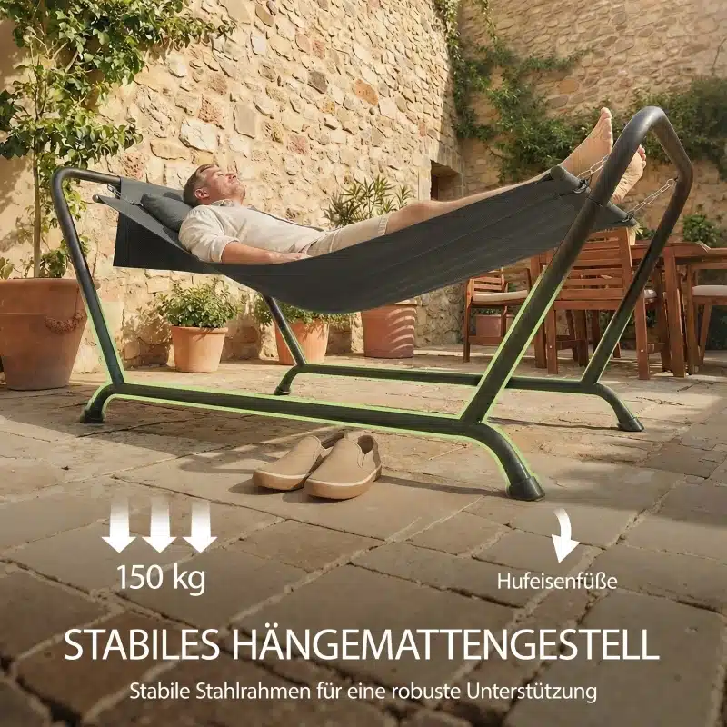 Rippvoodi aeda küljetasku ja peatoega 237x90 cm, kuue raamiga metallalusel, mis on paigaldatud kiviplaatidest terrassile. Päikesevalguse käes lõõgastuv inimene lamab mugavalt voodis, taustal kivisein ja taimed potis.