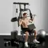 Jõusaali jõujaam 45kg raskusega koduseks treeninguks | E-pood Tootemaailm Treeningvarustuse komplekt Jõusaali jõujaam 45kg raskusega koduseks treeninguks, millel on mees treenimas musta terasest ja puidust masina taustal neutraalse värviga sein.
