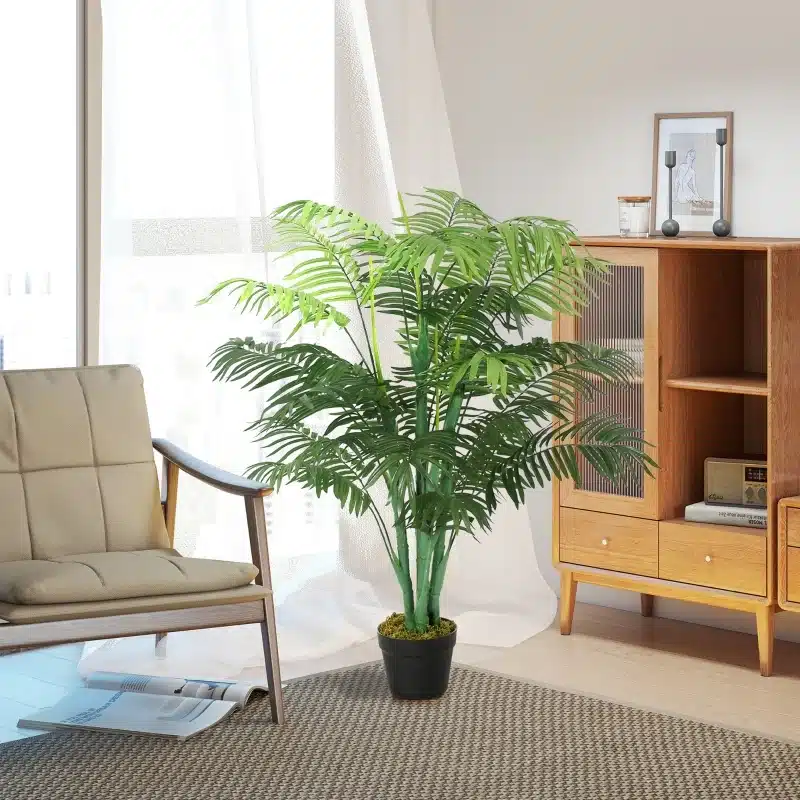 Kunstpalm 125 cm kõrguse dekoratiivse rohestikuga potis, seiseb elegantselt heledas elutoas vaiba peal ja kõrval asetseb modernse disainiga tugitool ja puidust kapp.