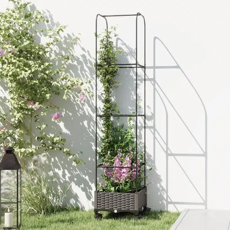 Kõrge aiakast trellisega ratastel, äravooluavaga 40x40x185, metallraamiga ja täidetud õitsevate taimedega, seisab rohelisel murul valge seina taustal, kõrval latern.