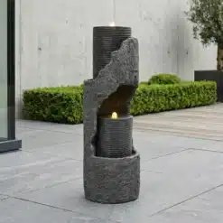 Hall kunstkivist aia purskkaev koos LED valgustusega, seistes modernse betoonterrassi keskel, ümbritsetuna rohelisest taimestikust.