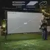 Projektoriekraan 100" 4K kahepoolne kokkupandav statiiviga | E-pood Tootemaailm Öine aias, suur 100-tolline 4K kaksikkülgne projektoriekraan statiiviga. Musta raamiga ekraan on muruplatsil üles seatud koos mõõtude joonistega, mille kõrval seisab inimene, andes suuruse võrdluse.
