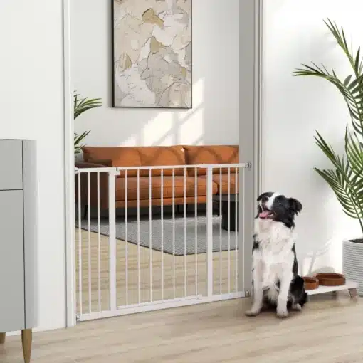 Lemmiklooma turvavärav trepile, metall, valge, 76–107 cm | E-pood Tootemaailm Valge metallist lemmiklooma turvavärav trepile, kõrgusega 76–107 cm, paigaldatud siseuksele. Läheduses istub koer, taustal on moodne elutuba oranži diivaniga.