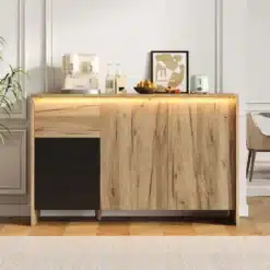 Puidust disain kummut LED valgustusega, mõõtudega 120x76x40 cm, seisab elegantselt elutoas helebeeži seinaga taustal. Kummuti peal on kaasaegsed dekoratiivesemed nagu mahlapress, pudelid ja abstraktne kunstiteos.