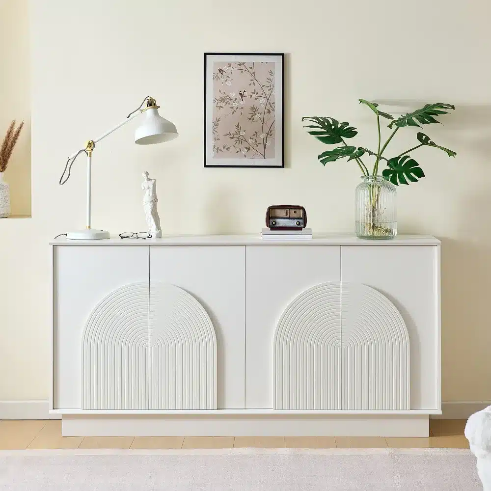 Valge kummut 160 cm matt viimistlus ja kaarjate ustega, minimalistlik disain, valgel puidust põrandal heleda seina taustal, koos dekoreerivate elementidega nagu lamp, vaas ja pilt seinas.