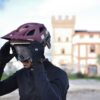 Maastikukiiver sinine suurus L matt viimistlusega | E-pood Tootemaailm Mees paneb selga lilla jalgrattakiivrit ja prille, taustal hoone