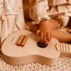 Laste ukulele mängupill 4 keelega alates 3. eluaastast | E-pood Tootemaailm Lapse käsi mängib heledal ukulelel kootud pleedi peal