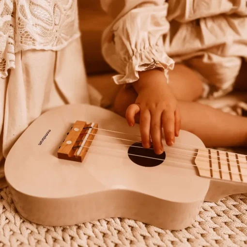 Laste ukulele mängupill 4 keelega alates 3. eluaastast | E-pood Tootemaailm Lapse käsi mängib heledal ukulelel kootud pleedi peal