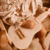 Laste ukulele mängupill 4 keelega alates 3. eluaastast | E-pood Tootemaailm Laps hoiab heledat väikest keelpilli süles ja mängib sellega