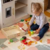 Puidust puu- ja köögiviljade lõikamise mängukomplekt 17-osaline | E-pood Tootemaailm Väikelaps mängib põrandal värviliste puuvilja- ja köögiviljamänguasjadega