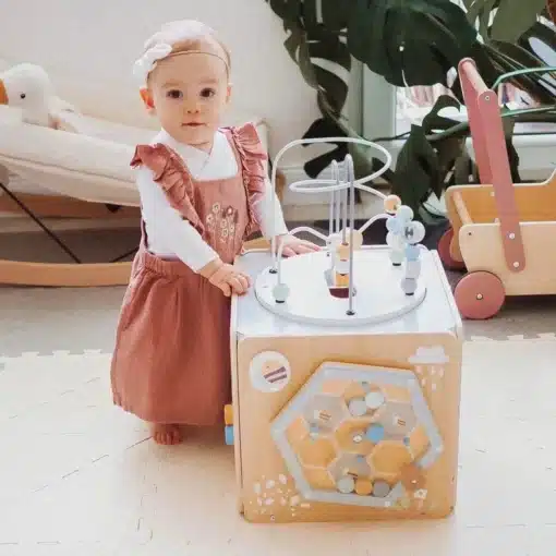 Montessori tegeluskuubik lastele 12+ kuud | E-pood Tootemaailm Väikelaps seisab mängutoa puidust tegevuskeskuse kõrval ja mängib selle erinevate elementidega