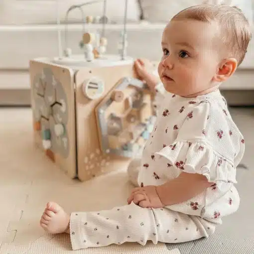 Montessori tegeluskuubik lastele 12+ kuud | E-pood Tootemaailm Beebi istub põrandal lillelises riietuses mängukasti kõrval