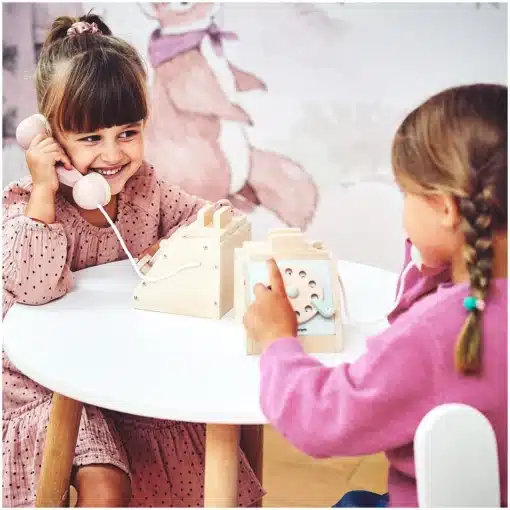 Montessori mängutelefon lastele 3+ | E-pood Tootemaailm Kaks tüdrukut mängivad laua taga mänguasjatelefoniga