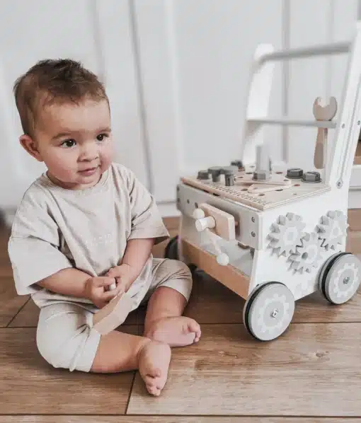 Puidust 3in1 käimistugi ja töölaud 47 osaga Montessori mänguasi | E-pood Tootemaailm Väikelaps istub põrandal ja mängib puidust tegevuskeskuse või lükatava mänguasjaga.
