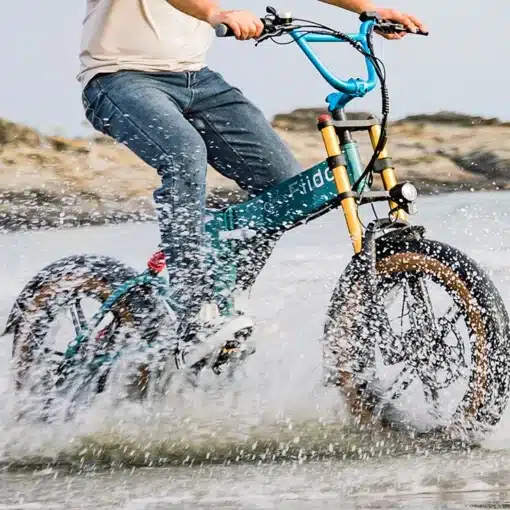 Kokkupandav elektrijalgratas Fiido M1 Pro roheline | E-pood Tootemaailm Inimene sõidab läbi vee fatbike-tüüpi elektrirattaga, pritsmed lendavad ümber ratta