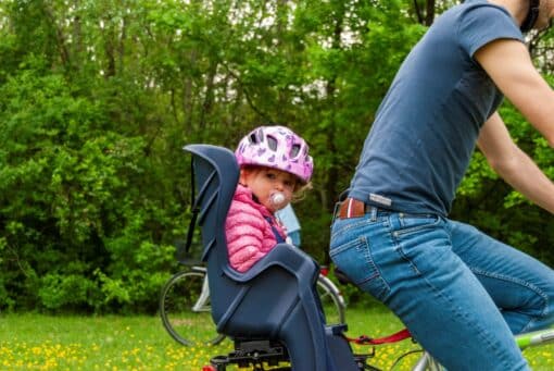 Laps kiiver peas istub jalgratta lastetoolis koos täiskasvanuga sõitval rattal