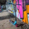 Trikitõukeratas Soke Go türkiissinine | E-pood Tootemaailm Graffiti tausta ees seisab sinine ja must trikitõukeratas roosade ratastega
