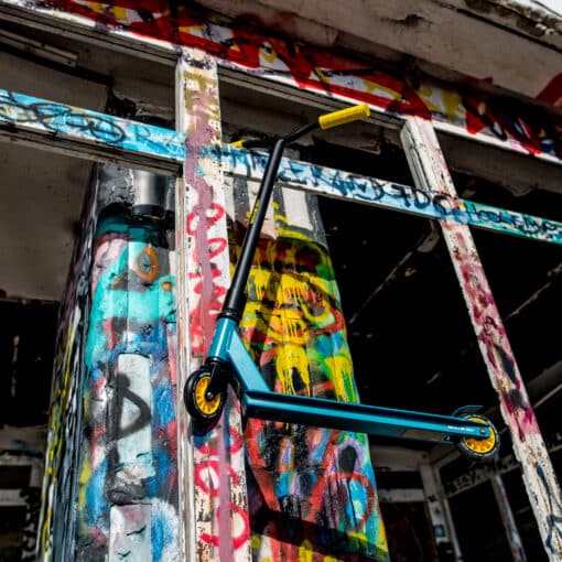 Trikitõukeratas Soke Go sinine-kollane | E-pood Tootemaailm Sinine trikitõukeratas värvilise grafitiseina ja lagunenud hoone taustal