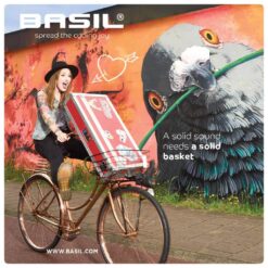 Naine sõidab jalgrattaga, ees korvis punane BASIL pagasikohver; taustal BASIL reklaamgraffiti ja papagoi kujutis