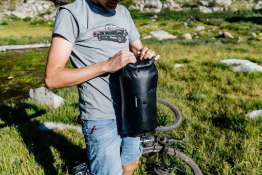 Lenksukott Giant H2Pro veekindel 12,5 l | E-pood Tootemaailm Mees pakib musta veekindlat kandekotti õues rohumaal, jalgratas taustal