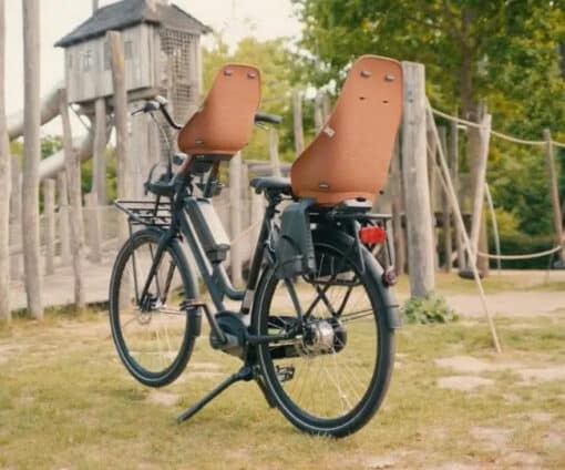 Laste jalgrattatool Urban Iki Bio pakiraamile | E-pood Tootemaailm Kaks elektrijalgratast lapseistmetega pargis puidust mänguala taustal