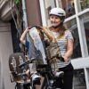 Jalgratta lastetool Urban Iki Ta-ke | E-pood Tootemaailm Naine jalgrattakiivris juhib last jalgratta lastetoolis vihmakattega