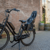 Laste jalgrattatool Urban Iki Ta-ke pakiraamile | E-pood Tootemaailm Must elektriratas lastetooliga telliskiviseina ääres