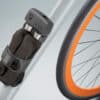 Lülilukk AXA Foldable 1000 105 cm | E-pood Tootemaailm Jalgratta raami külge kinnitatud must turvalukk oranži rattarummu kõrval